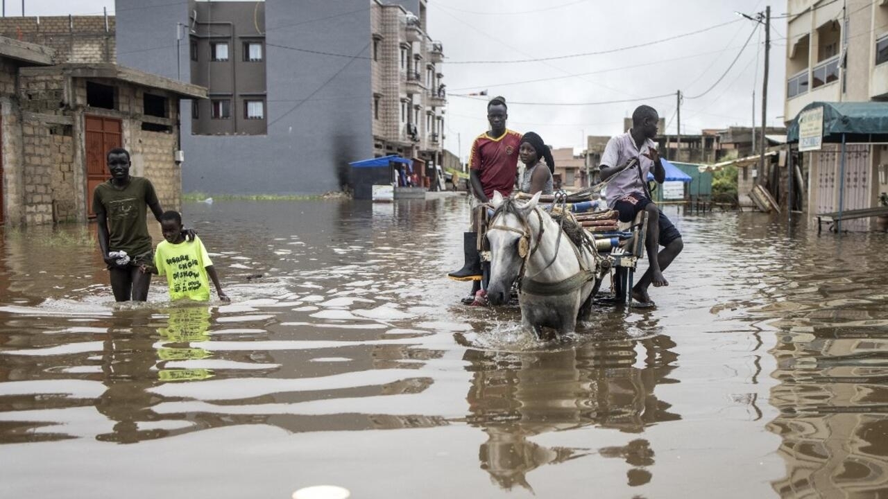 People make their way through the flooded neighbourhood of Keur Massar, Dakar, on August 20, 2021. - Each year the neighbourhood of Keur Massar deals with heavy flooding during the peak of the rainy season. Families living in Keur Massar pack up their belongings and move out of the area during this period. Last year, after the worst flooding to date, the government gave over fifteen million West African Francs towards a project to help fight the flooding and displacement in this area. (Photo by JOHN WESSELS / AFP)